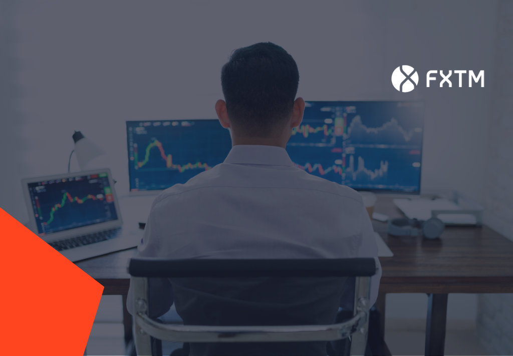 back of mans head sat at a desk looking at screens with candlestick charts